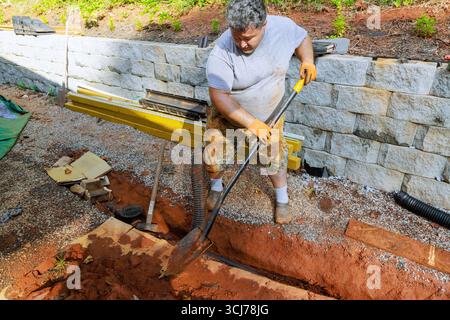 Laborer uses shovel to dig trench in garden for an outdoor new drainage system project on work day. Stock Photo