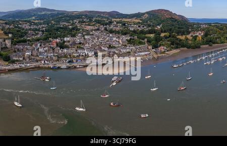 Aerial Image of Conwy, Wales, with town walls, waterfront, and boats moored along the estuary on a bright summer day. Stock Photo