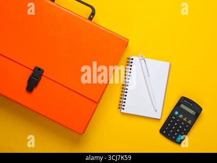 Orange paper case, notebook and calculator on a yellow background. Top view Stock Photo
