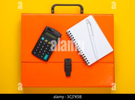 Orange paper case, notebook and calculator on a yellow background. Top view Stock Photo