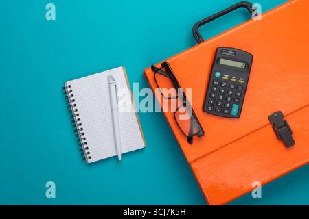 Orange paper case, notebook and calculator on a blue background. Top view Stock Photo