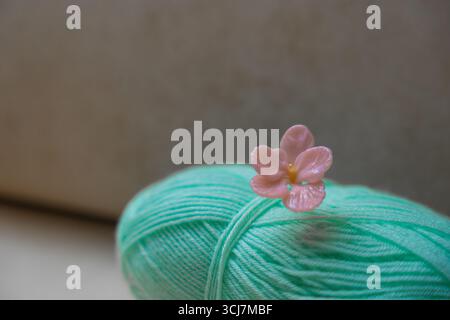 Mint green yarn ball with handmade pink glass flower pin on soft neutral background, copy space Stock Photo