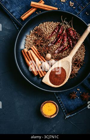 Mixed organic spices (coriander, nutmeg, anise stars, cayenne pepper,  turmeric, paprika,  cinnamon sticks) on ceramic plate on black background, top Stock Photo