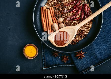 Mixed organic spices (coriander, nutmeg, anise stars, cayenne pepper,  turmeric, paprika,  cinnamon sticks) on ceramic plate on black background, top Stock Photo