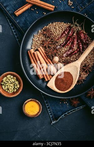 Mixed organic spices (coriander, nutmeg, anise stars, cayenne pepper,  turmeric, paprika,  cinnamon sticks) on ceramic plate on black background, top Stock Photo