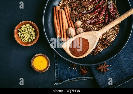 Mixed organic spices (coriander, nutmeg, anise stars, cayenne pepper,  turmeric, paprika,  cinnamon sticks) on ceramic plate on black background, top Stock Photo