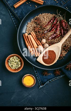 Mixed organic spices (coriander, nutmeg, anise stars, cayenne pepper,  turmeric, paprika,  cinnamon sticks) on ceramic plate on black background, top Stock Photo