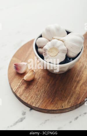 Garlic Cloves and Bulb in ceramic bowl on wooden cutting board closeup Stock Photo