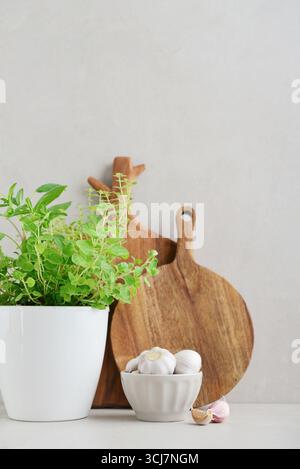 Fresh seasoning herbs in flower pot, two wooden cutting board and garlic cloves and bulb on light background Stock Photo