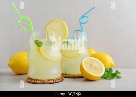 Two glasses of homemade lemonade with drinking straws,  fresh lemons and mint on light background Stock Photo