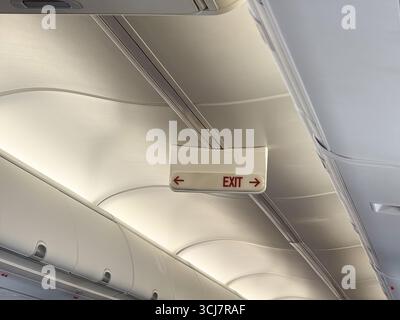 An illuminated airplane exit sign with red lettering and directional arrows on the cabin ceiling. Safety, travel, and the importance of guidance Stock Photo