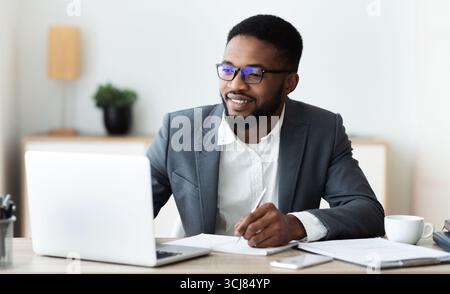 Handsome black entrepreneur working on laptop and taking notes Stock Photo