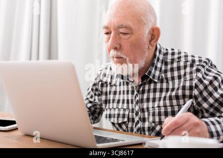 Mature man using laptop and writing in notepad Stock Photo