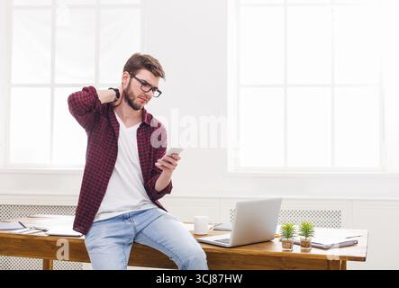 Tired, overworking businessman using mobile phone in modern white office Stock Photo