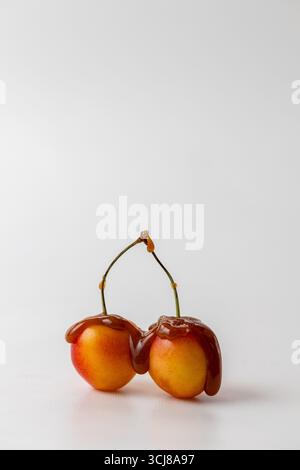 two Rainier Cherries drizzled with caramel sauce on a white background, vertical image with copyspace Stock Photo