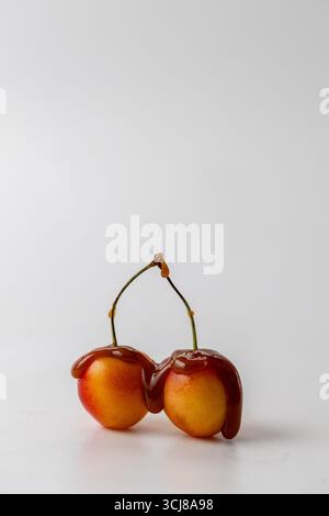 two Rainier Cherries drizzled with caramel sauce on a white background, vertical image with copyspace Stock Photo