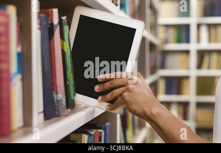 Afro student placing digital tablet on bookshelf Stock Photo