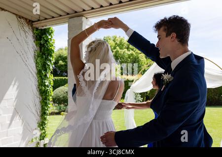 Dancing joyfully outdoors, bride and groom celebrating wedding with guests Stock Photo