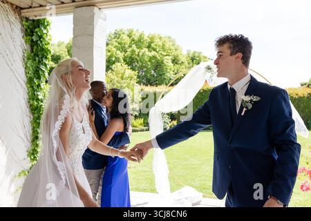 Bride and groom joyfully dancing outdoors, celebrating wedding with friends Stock Photo