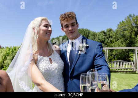 Bride and groom celebrating outdoors, smiling and holding champagne glasses Stock Photo
