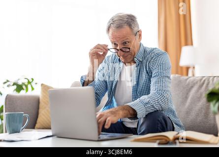 Surprised mature man using laptop looking at screen Stock Photo
