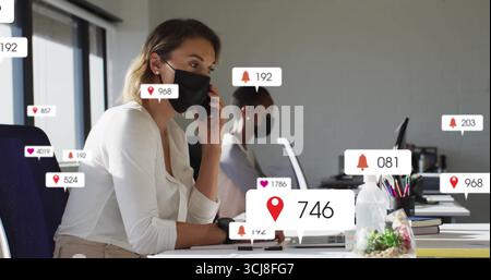 Holding smartphone to ear, woman wearing black face mask at office with notifications, copy space Stock Photo