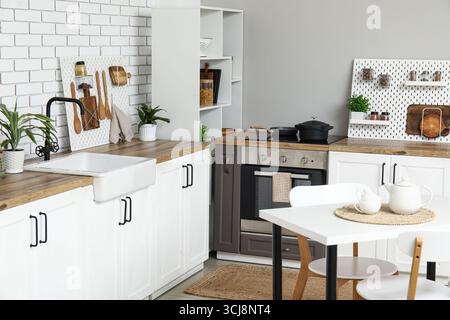Stylish light kitchen with pegboards and modern dining table Stock Photo