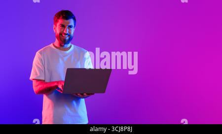 Young caucasian guy using laptop in studio with neon light Stock Photo