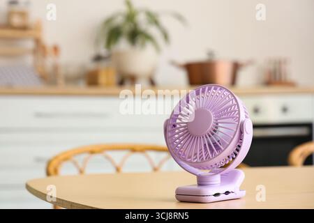 Lilac mini fan on table in kitchen, closeup Stock Photo