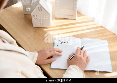 Young woman writing New Year goals at home, closeup Stock Photo