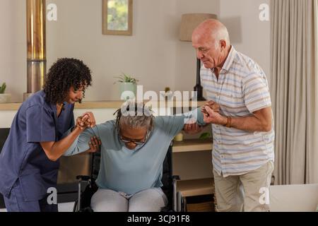 Caregiver and senior man assisting elderly woman from wheelchair at home Stock Photo