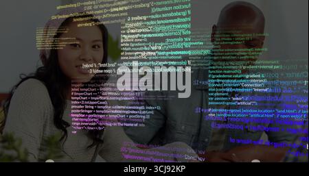 Collaborating software team leaning around tech desk, laptop coffee-cup plant papers code overlay Stock Photo