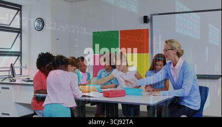 Guiding teacher leaning over school table helping students with writing and drawing using notebooks Stock Photo
