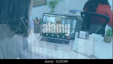 Showing colleague waving on laptop screen in open-plan office, with pencil holder and sticky notes Stock Photo