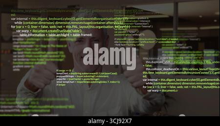 Standing mature developer smiling and holding thumbs up in office, overlaying HTML JavaScript code Stock Photo