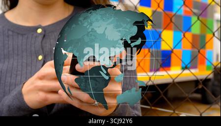 Holding smartphone, man in grey sweater displaying globe overlay at chainlink fence, colorful mural Stock Photo