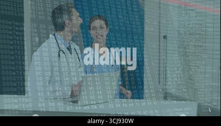 Two doctors in scrubs discussing data in hospital room, with monitors and stethoscopes Stock Photo