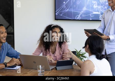 In office, diverse team collaborating using laptops and tablets in meeting Stock Photo