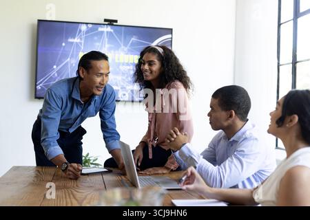 Diverse business team collaborating in modern office, discussing project on laptop Stock Photo