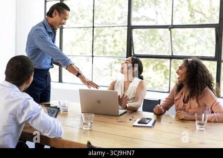 In meeting, diverse team discussing ideas around laptop, collaborating and smiling Stock Photo