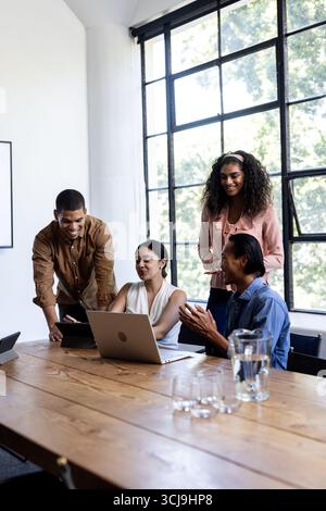 Diverse business team collaborating on laptop in modern office, smiling and engaged Stock Photo