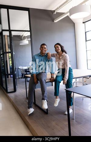 Smiling colleagues in modern office, sitting on desk, enjoying teamwork Stock Photo