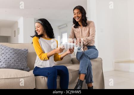 Mother and daughter sitting on sofa, reading letter together, smiling happily Stock Photo