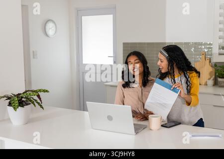 Smiling women discussing document at home with laptop and coffee on table Stock Photo