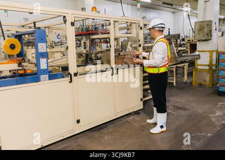 A worker in a helmet and safety vest operates machinery in an industrial setting, emphasizing workplace safety and the importance of machinery in prod Stock Photo