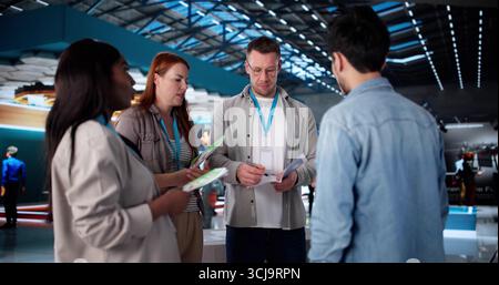Busy Team Of Diverse Employees At Technology Showcase In Convention Hall. Stock Photo