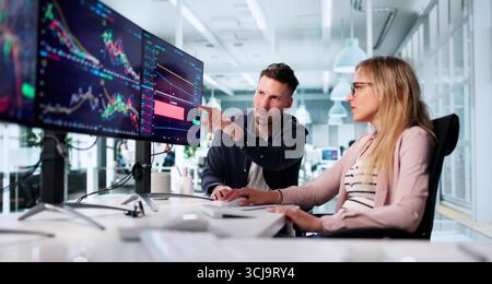 Financial Broker Analyzing Data On Multiple Computer Screens In Office Stock Photo