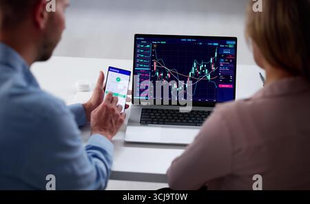 Young Couple Trading Stock Market Exchange On Laptop In Office. Business Brokers Working Together Stock Photo