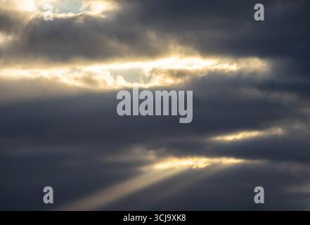 Rays of sunlight breaking through heavy dark clouds in the sky Stock Photo