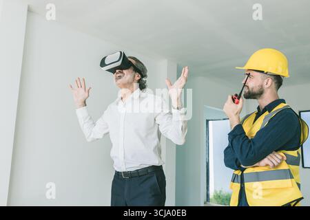 Construction manager happy exciting using VR visual reality presentation technology device present by builder at home contraction site Stock Photo